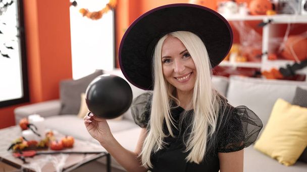 Young blonde woman wearing witch costume holding balloon at home - Φωτογραφία, εικόνα