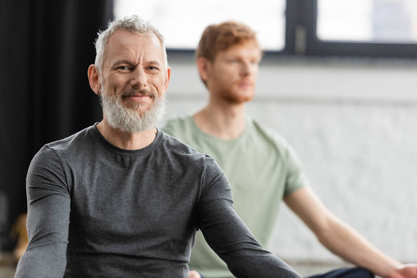 Bearded middle aged man smiling at camera in yoga studio  - Fotografie, Obrázek