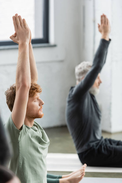 Young redhead man doing anjali mudra while sitting in yoga class  - Photo, Image