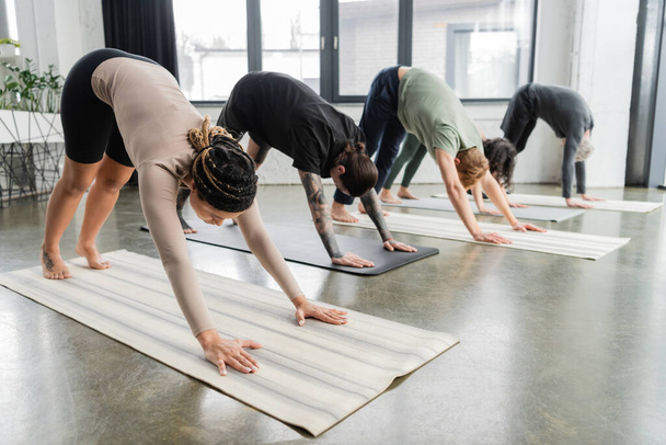 Young african american woman doing Downward Facing Dog asana in group in yoga class  - Photo, Image