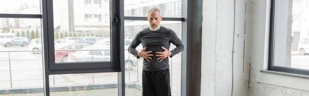 Mature man in sportswear touching belly while practicing yoga in class, banner  - Photo, Image
