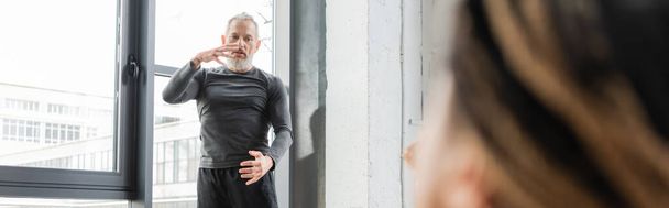 Mature coach explaining asana to blurred african american woman in yoga class, banner  - Photo, image