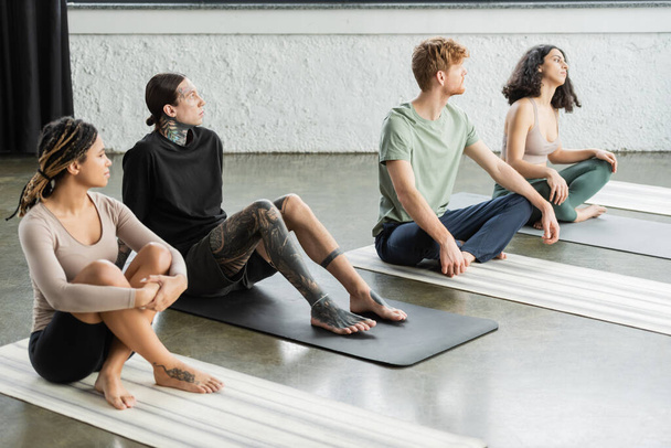 Young interracial people sitting on mats in yoga studio  - Foto, imagen