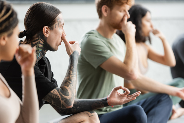 Tattooed man practicing nostril breathing and gyan mudra in yoga class  - Photo, Image