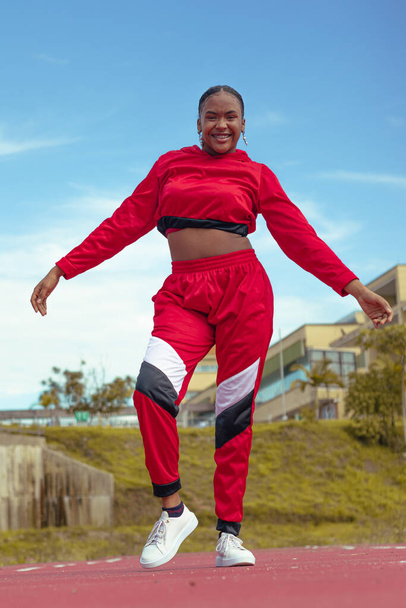 Mujer afro bailarina realiza baile en parque local en la pista de atletismo con hermosa vegetacion y cielo de fondo - Foto, immagini
