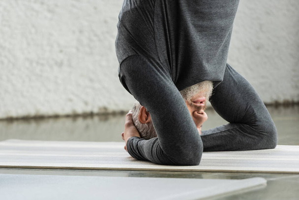 Dojrzały mężczyzna robi Supported Headstand asana na macie w studio jogi  - Zdjęcie, obraz
