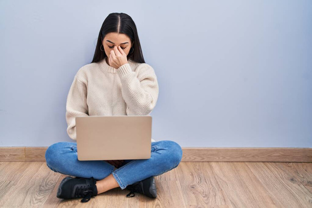 Νεαρή γυναίκα που χρησιμοποιεί φορητό υπολογιστή κάθεται στο πάτωμα στο σπίτι κουρασμένος τρίψιμο μύτη και τα μάτια αίσθημα κόπωσης και πονοκέφαλο. άγχος και απογοήτευση έννοια.  - Φωτογραφία, εικόνα