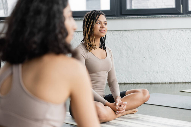 Smiling african american woman sitting on mat in yoga studio  - Photo, Image