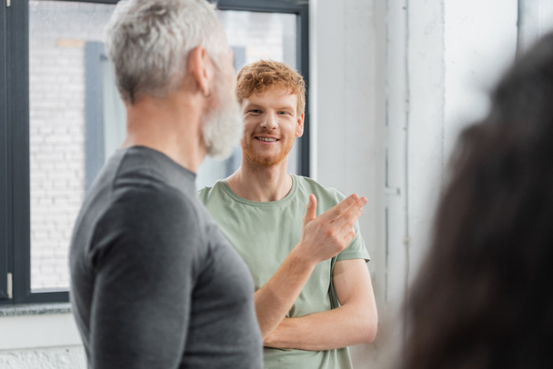 Smiling redhead man talking to blurred coach in yoga class  - Фото, изображение