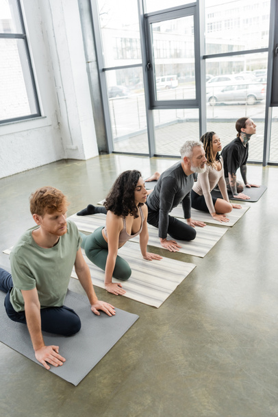 Interracial group of people practicing Half Pigeon asana with closed eyes in yoga class  - Foto, Bild