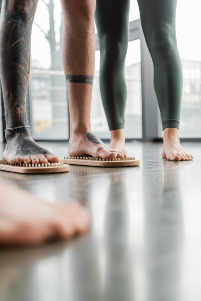 обрізаний вид татуйованого чоловіка, що стоїть з голими ногами на дошці для нігтів біля жінки в студії йоги
 - Фото, зображення