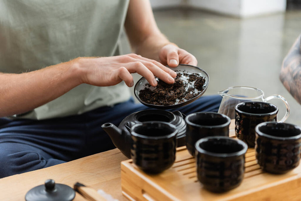 bijgesneden weergave van de mens het toevoegen van zuiverder thee in traditionele Japanse theepot in de buurt van cups  - Foto, afbeelding