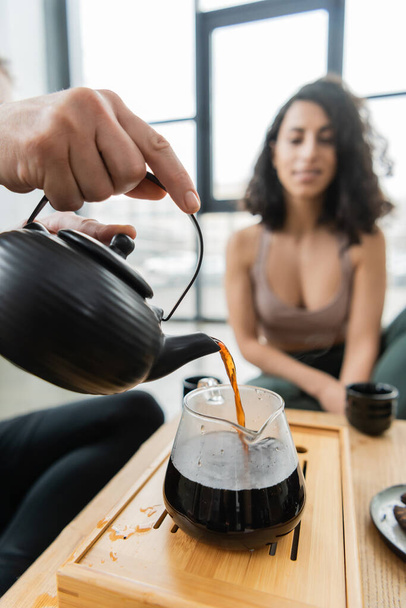 man pouring brewed puer tea into glass jug near middle eastern woman on blurred background  - Foto, Bild