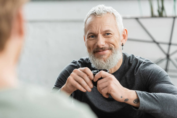 šťastný muž středního věku s tetováním drží čínský šálek s puer čaj v jóga studiu  - Fotografie, Obrázek