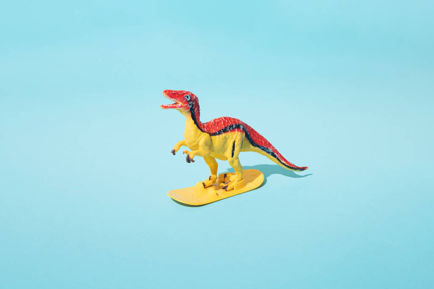 Dinosaurio surfeando sobre un fondo azul. - Foto, imagen