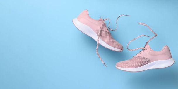 Pink women's sports sneakers with laces levitate on a blue background. Copy space - Fotoğraf, Görsel