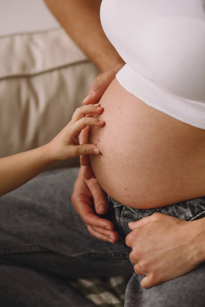 Zwangere vrouw, haar man en hun kind houden hun handen op een zwangere buik. Liefdesconcept. Het concept van gelukkig moederschap en ouderschap - Foto, afbeelding