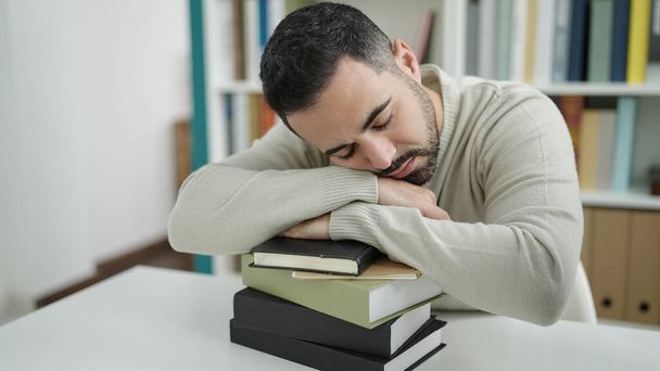 Young hispanic man student sleeping with head on books at library university - Foto, afbeelding