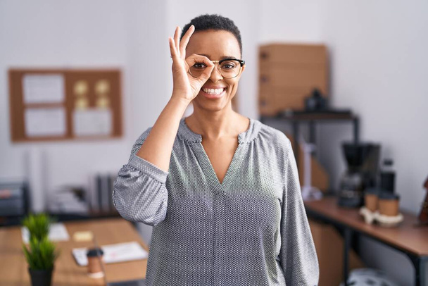 Africano americano mulher trabalhando no escritório usando óculos fazendo ok gesto com a mão sorrindo, olho olhando através dos dedos com o rosto feliz.  - Foto, Imagem