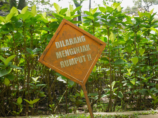 a warning sign prohibiting stepping on grass in a park written in Indonesian - Photo, Image