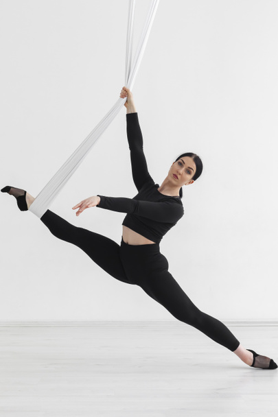 Female in black tights. Professional aerial performer. Inverted anti-gravity Aerial yoga with the use of aerial silks or fabrics, Balance between physical and mental effort concept. Isolated on white. - Φωτογραφία, εικόνα