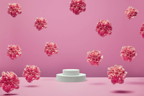 white round podium for presentation products and cosmetics with fresh pastel flowers flying in the air on pink background. - Foto, afbeelding