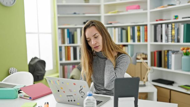 Kütüphane üniversitesinde okuyan genç, beyaz bir kız öğrenci dizüstü bilgisayar ve dokunmatik ped kullanıyor. - Fotoğraf, Görsel