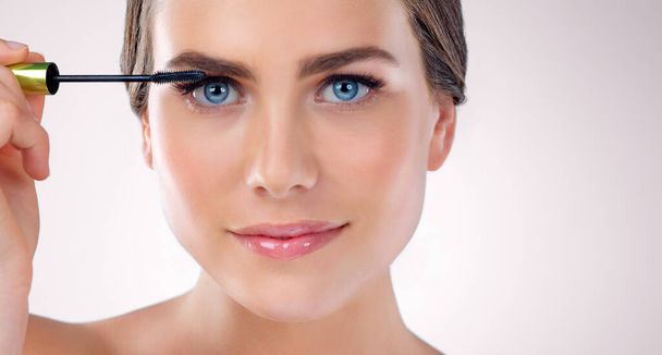 Schöne Wimpern. Studioaufnahme einer attraktiven Frau, die Mascara vor grauem Hintergrund aufträgt - Foto, Bild