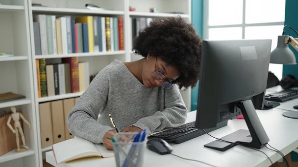 アフリカ系アメリカ人の女子学生が図書館大学のノートにコンピュータ・ライティングを使って - 写真・画像