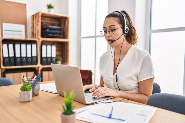 Young hispanic woman wearing call center agent headset at the office scared and amazed with open mouth for surprise, disbelief face  - Fotografie, Obrázek