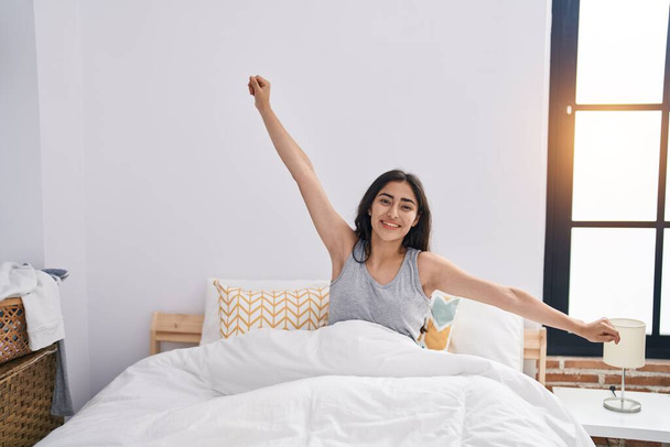 Νεαρό ισπανόφωνο κορίτσι χαμογελά αυτοπεποίθηση ξυπνώντας στο υπνοδωμάτιο - Φωτογραφία, εικόνα
