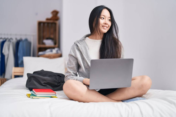Jeune femme chinoise à l'aide d'un ordinateur portable étudier sur le lit dans la chambre - Photo, image
