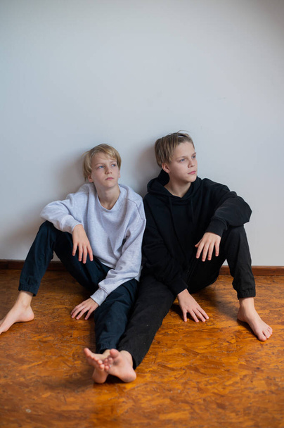 Two happy boys, happy brothers who are seriosly happily together. Brothers stay on grey background. modern tenagers.book cover. one boy in focus other out of focus - Foto, Imagem