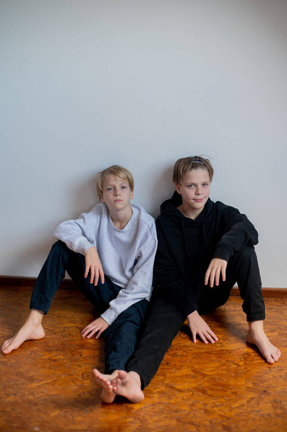 Two happy boys, happy brothers who are seriosly happily together. Brothers stay on grey background. modern tenagers.book cover. one boy in focus other out of focus - Photo, Image