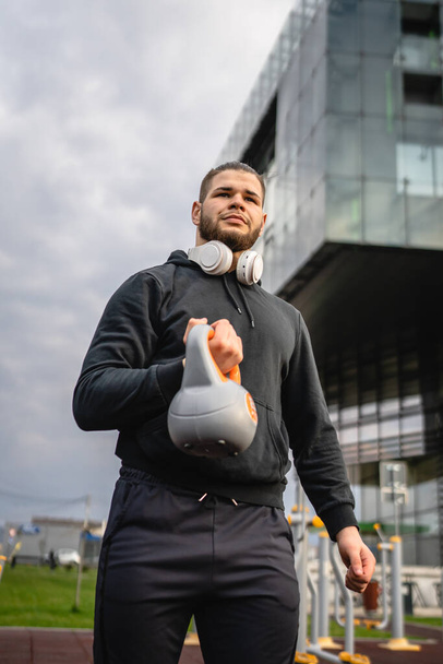 Un homme jeune athlète masculin caucasien debout en plein air dans la journée posant avec la cloche russe girya kettlebell poids espace de copie personne réelle - Photo, image
