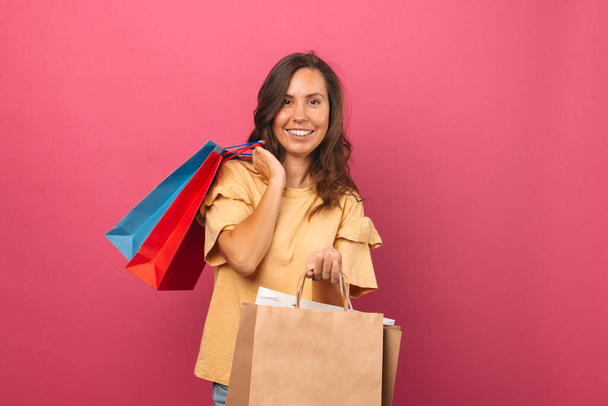 Веселая молодая улыбающаяся женщина держит несколько мешков для покупок на розовом фоне. - Фото, изображение