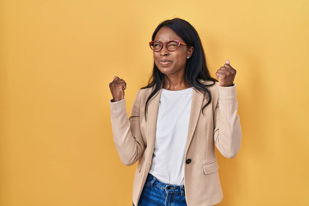 Mulher jovem africana usando óculos muito feliz e animado fazendo gesto vencedor com os braços levantados, sorrindo e gritando para o sucesso. conceito de celebração.  - Foto, Imagem