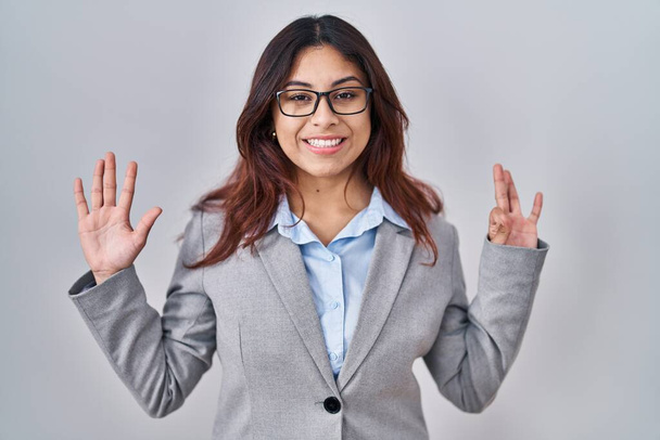 Hispánská mladá obchodní žena nosí brýle ukazující a ukazující nahoru prsty číslo osm a zároveň se usmívá sebevědomě a šťastně.  - Fotografie, Obrázek