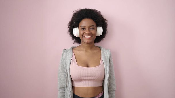 Afroamerikanerin lächelt selbstbewusst und hört Musik vor isoliertem rosa Hintergrund - Foto, Bild