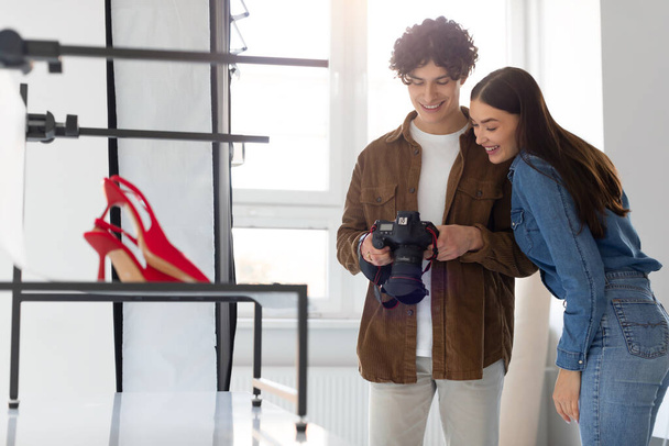 Tiimi ammattivalokuvaaja ja naispuolinen taideohjaaja tarkkailun kuvia moderni valokamera tehdessään sisältöä kuvauksen, seisoo lähellä punainen tyylikäs kengät - Valokuva, kuva
