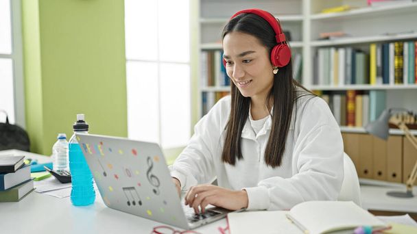 Young beautiful hispanic woman student using laptop and headphones studying at university classroom - Fotoğraf, Görsel