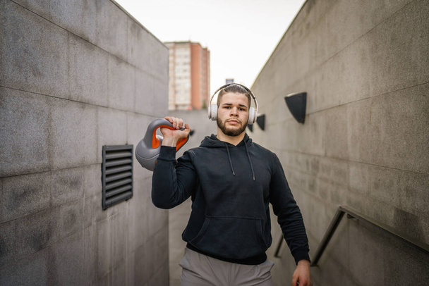 Ein Mann junge kaukasische männliche Sportler stehen im Freien in Tagestraining mit russischer Glocke girya Kettlebell Gewichtsübung echte Person Kopierraum - Foto, Bild