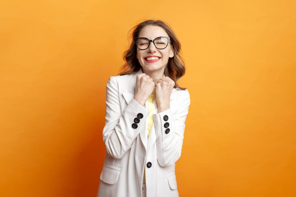young business girl in glasses and white suit celebrating victory on colored isolated background, woman manager in blazer wins and shows gesture of success - 写真・画像