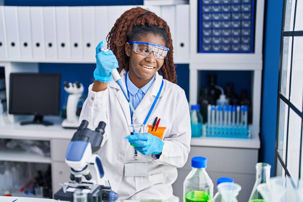 Африканська американська жінка - науковець, яка виливає рідину на пробірку в лабораторії. - Фото, зображення