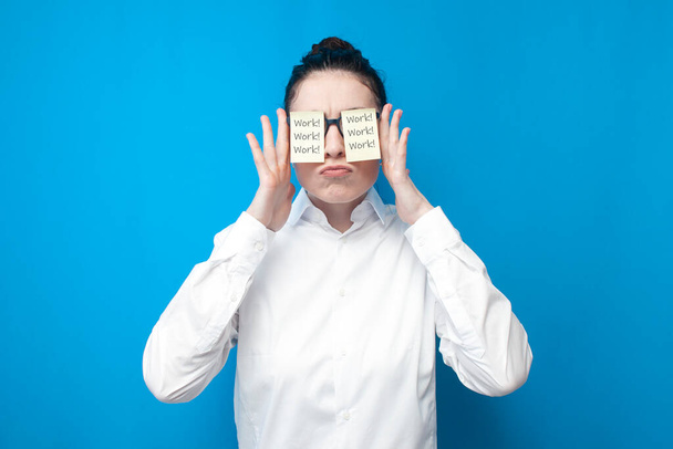 cheerful girl manager in white shirt with blank papers in front of her eyes smiles on blue background, woman office worker in glasses on colored background - Foto, Imagen