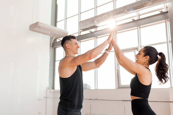 beautiful athletic couple in sportswear greet each other in the gym in the morning, fitness girl and coach man give high five in training in bright room - Zdjęcie, obraz
