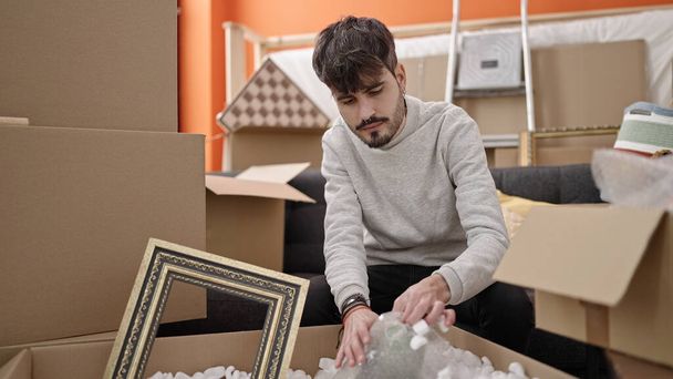 Young hispanic man unpacking cardboard box at new home - Zdjęcie, obraz