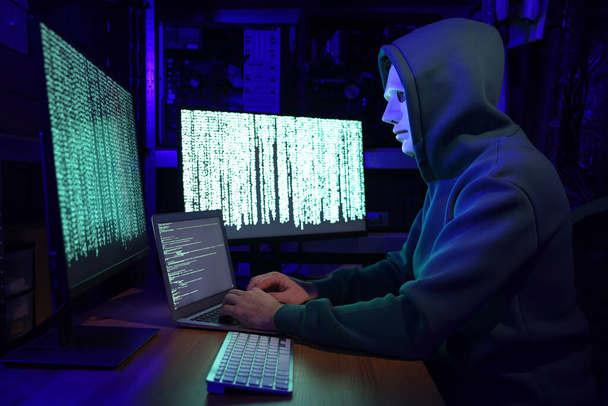 Hacker in mask working with computers in dark room. Cyber attack - Foto, afbeelding
