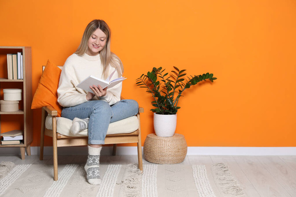 Young woman reading book in armchair at home, space for text. Interior design - Foto, afbeelding