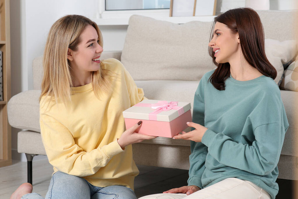 Smiling young woman presenting gift to her friend at home - Photo, Image